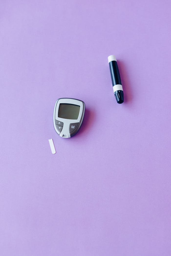 about-me-02 Flat lay of glucose monitor and lancet on a purple background for diabetes management.