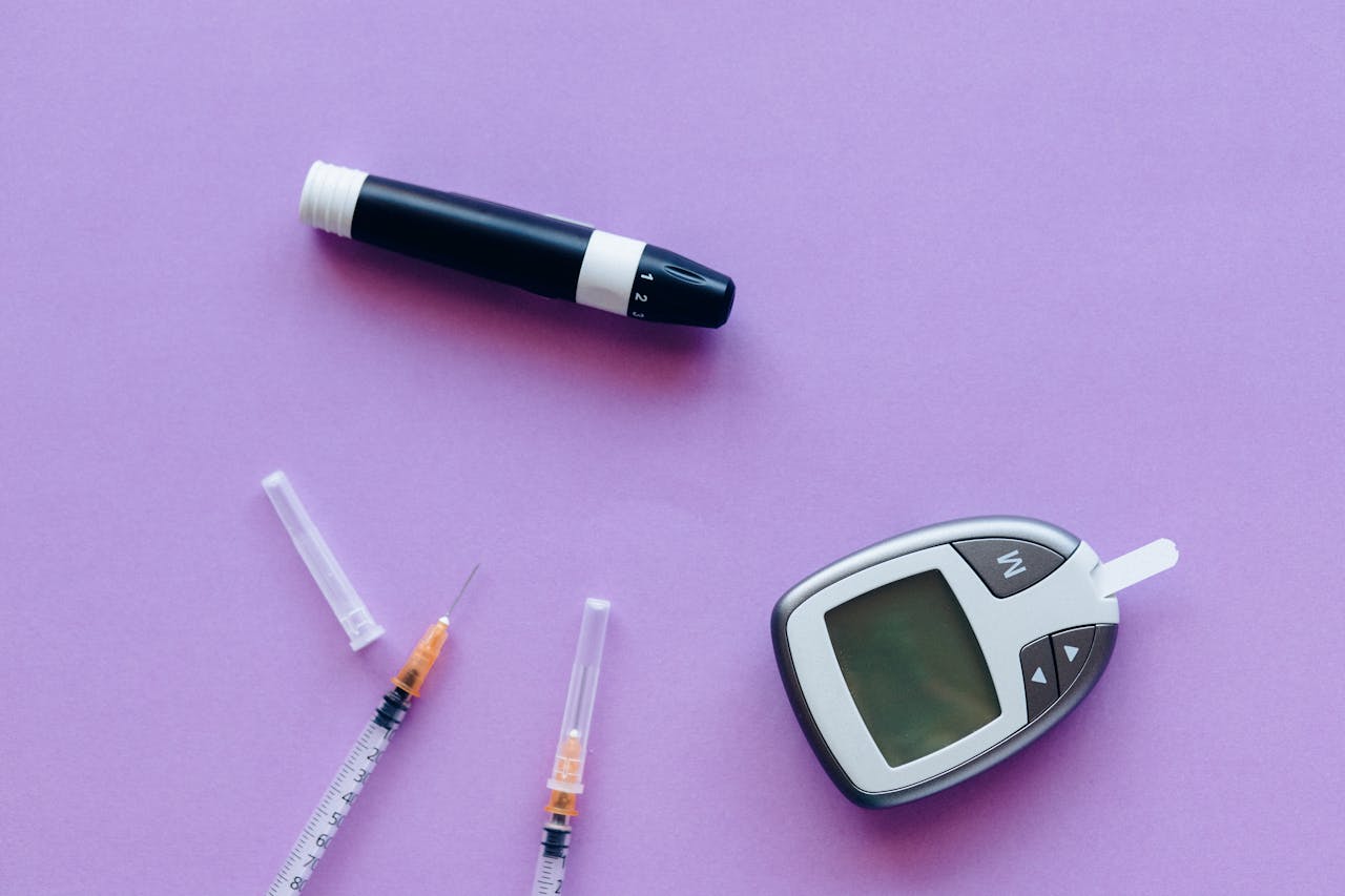 service-05 Top view of diabetes management tools including glucose meter and insulin syringes on purple background.